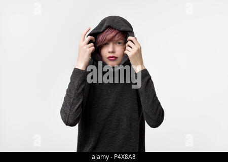 Portrait of unusual informal pretty woman with colorful hairstyle. She is pulling up hood and look confident. Concept od self expression. Stock Photo