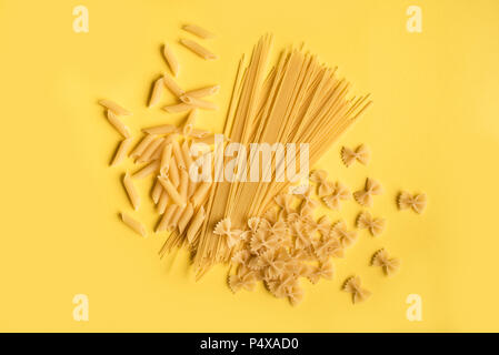Assorted various uncooked raw pasta on yellow background. Italian pasta: penne, farfalle, spaghetti. Stock Photo