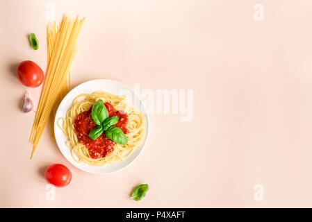 Spaghetti pasta bolognese and ingredients on pink background, top view. Plate of pasta dish with tomato sauce and basil, creative pastel background. Stock Photo