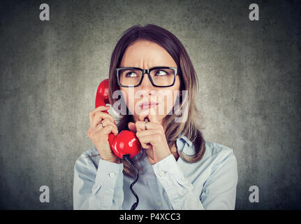 Young woman in shirt and glasses having call on telephone and frowning with confusion being concerned with problems Stock Photo
