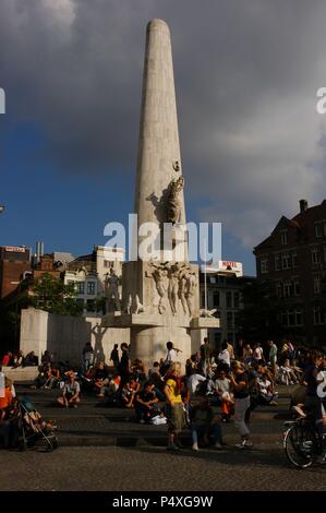 People sitting on Dam Square at the foot of the National Monument, obelisk erected in 1956 by J. J. P. Oud and John Raedecker, in tribute to the fallen soldiers in World War II. Amsterdam. Holland. Stock Photo