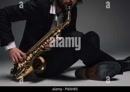 cropped shot of musician playing saxophone while sitting on floor Stock Photo