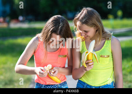 Two girl friends. Summer in nature. In hands of holding Bananas. The gestures of the hands clean the banana. The concept of eating in nature. Emotions happy smile. Stock Photo