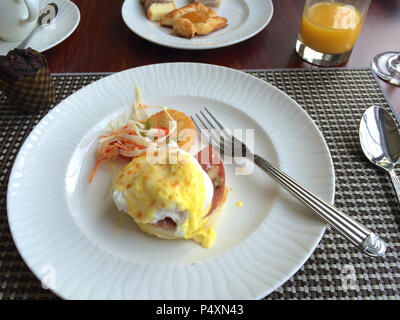 PULAU LANGKAWI, MALAYSIA - APR 6th 2015: Eggs Benedict is a traditional American breakfast or brunch dish with bacon, ham, a poached egg, and hollandaise sauce. Meal on a white plate in a luxury hotel restaurant Stock Photo