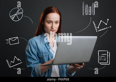 Confident programmer standing with a laptop and looking at the screen of it Stock Photo