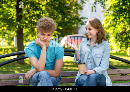 The man is tired of talking. The girl is talking to the guy. Unwillingness to listen to the interlocutor. A guy with a girl in summer in a park in nature. Problems in the relationship. Stock Photo