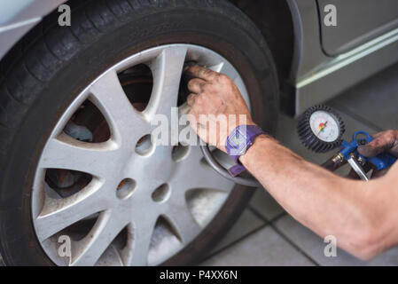 Closeup Of Mechanic At Repair Service Station Checking Tyre Pressure With Gauge Stock Photo