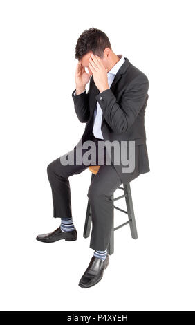 A tall man sitting in a dark suit with his hands on his face, is tired and depressed, isolated for white background Stock Photo
