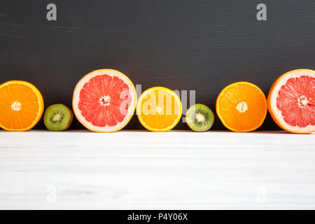 Sliced kiwi, orange, grapefruit and mandarin on black and white wooden background. Copy space. Summer background Stock Photo