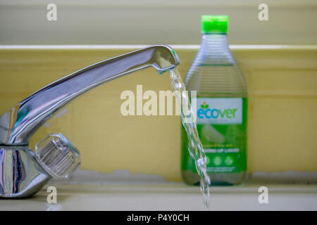 Running water from a kitchen tap with an ecological washing up liquid in the background Stock Photo
