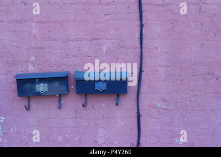 Antique distressed clay brick wall with peeling lavender painted surface displaying two old mailboxes and an electric cable Stock Photo