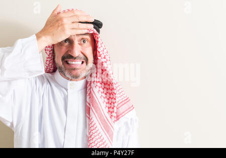 Senior arabic man stressed with hand on head, shocked with shame and surprise face, angry and frustrated. Fear and upset for mistake. Stock Photo