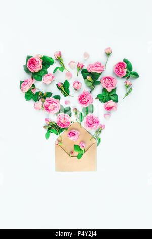 Close up creative layout with pink tea rose flowers,petals, leaves fly out of craft paper envelope in shape of heart on white background isolated. Spr Stock Photo