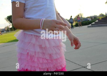 Toddler in white t-shirt and pink skirt, bracelets on hand. Stock Photo