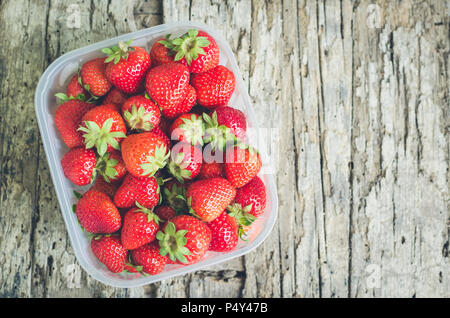 Background from freshly harvested strawberries. Box filled with succulent juicy fresh ripe red strawberries on an old wooden textured table top. Direc Stock Photo
