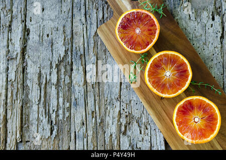 Sliced blood oranges with thyme on wooden board. Citrus background. Cut ripe juicy Sicilian Blood oranges fruits on old wooden textured background. To