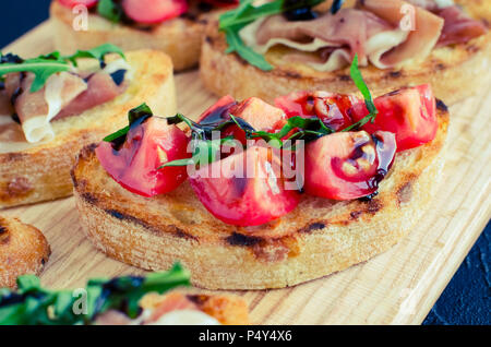 Selection of tasty Italian bruschetta or canapes on toasted baguette topped with tomatoes, Prosciutto di Parma, arugula and balsamic glasse sauce on c Stock Photo