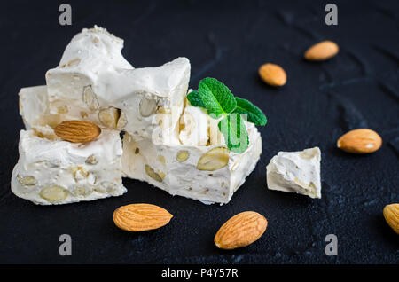 Sweet nougat with almonds on black stone background. Pieces of white nougat. Stock Photo