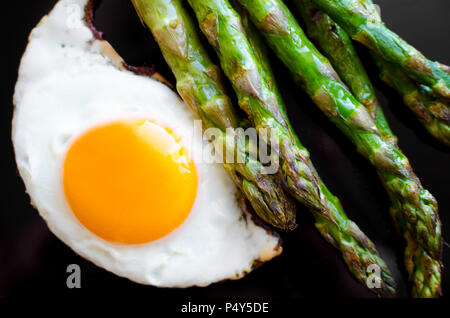 Fried egg and roasted fresh asparagus in black plate. Healthy lunch concept. Delicious, nutritious eating. Top view. Stock Photo