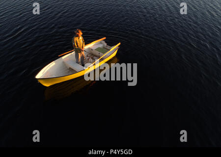 Lulea, Sweden - June 16, 2018: A man and his dog standing in a rowing boat fishing at sunset. Stock Photo