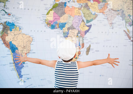 little child in captain hat spreading hands to world map Stock Photo