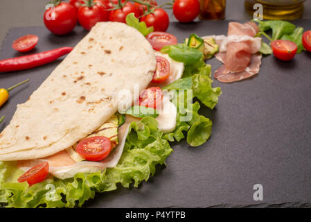 Italian piadina romagnola flatbread with lettuce, cherry tomatoes, prosciutto ham, mozzarella cheese and grilled zucchini Stock Photo