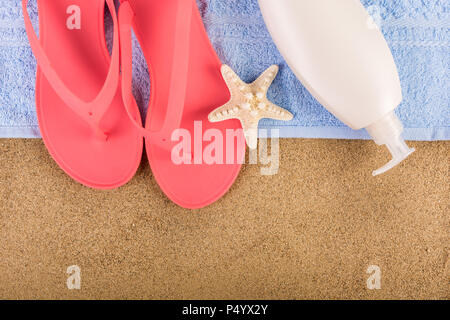 Pink sandal flip flop on blue towel and suntan cream lotion on sand beach and starfish. Summer vacations copy space and concept. Top view, close up Stock Photo