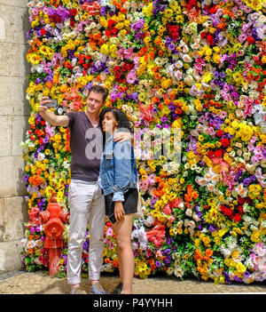 Young white man and beautiful black woman taking selfies before the colorful flowery wall Stock Photo