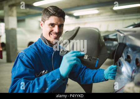 Portrait of smiling mechanic inspecting a car with a torch in a workshop Stock Photo