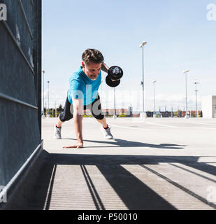 Man training with dumbells, doing one-armed plank Stock Photo