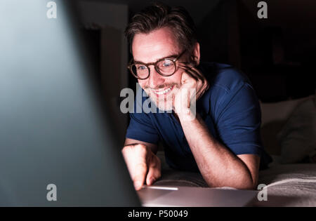 Portrait of smiling man lying on couch at home using laptop Stock Photo