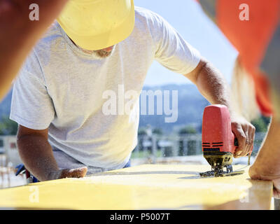 Construction worker cutting plywood with jigsaw on construction site Stock Photo