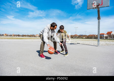 Father and son playing basketball on court outdoors Stock Photo