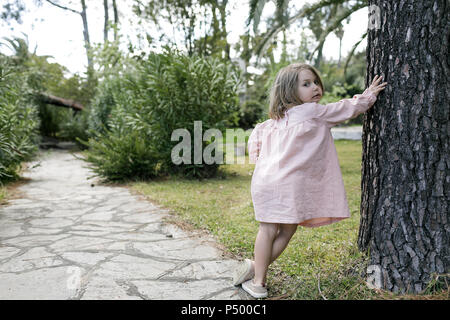 Portrait of little girl leaning against tree trunk in garden Stock Photo