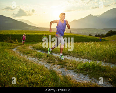 Athletes running on field path at sunset Stock Photo