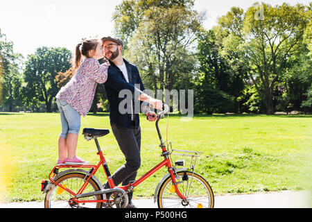 Daughter kissing father with bicycle in a park Stock Photo
