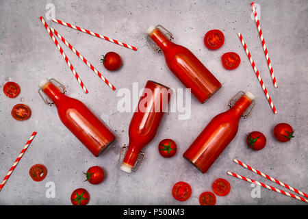 Homemade tomato juice in swing top bottles, straws and tomatoes on grey ground Stock Photo