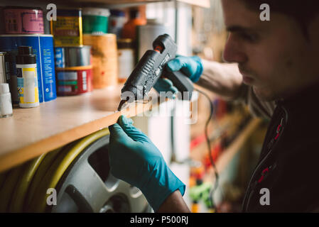 Man using a hot glue gun on shelf in workshop Stock Photo