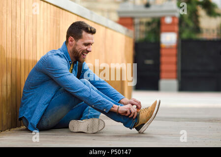 Young man laughing, sitting on footbridge Stock Photo