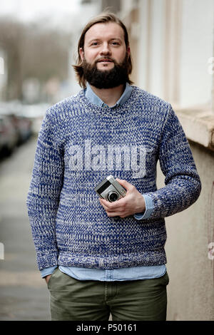 Man with beard standing in street, holding old camera Stock Photo