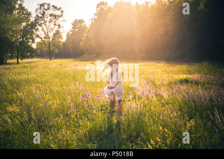 Back view of girl running on flower meadow at evening twilight Stock Photo