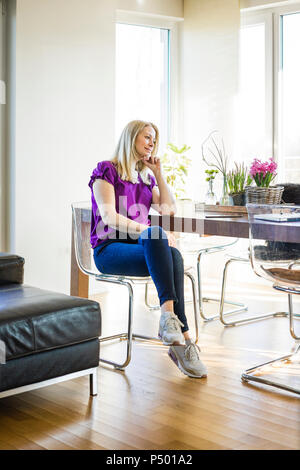 Pensive mature woman sitting at table at home Stock Photo