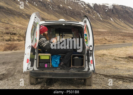 Iceland, man sitting in van using smartphone and laptop Stock Photo