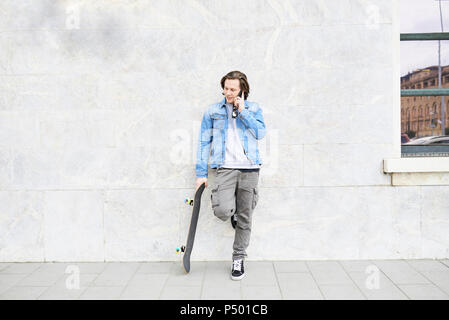 Young man holding skateboard, using smartphone Stock Photo