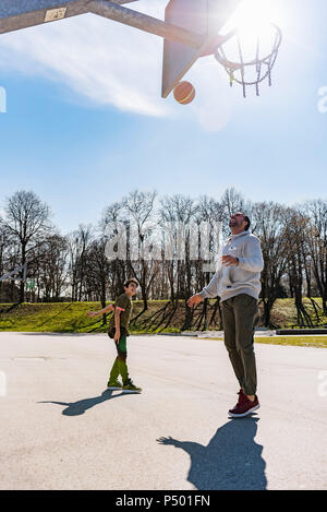 Father and son playing basketball on court outdoors Stock Photo