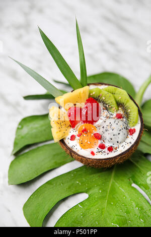 Coconut bowl with variuos fruits, natural yoghurt and seeds on leaf Stock Photo