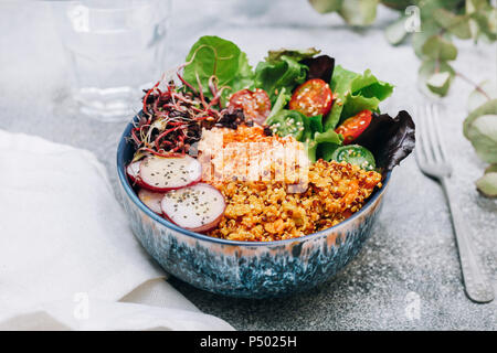 Vegan buddha bowl with hummus, quinoa with curry, lettuce, sprouts, green and red cherry tomatoes, sliced radish and sesame and poppy seeds Stock Photo