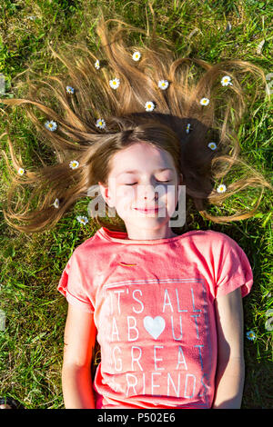Portrait of smiling girl lying on grass in spring with daisies on hair Stock Photo