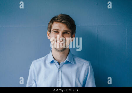 Portrait of smiling man in front of blue wall Stock Photo