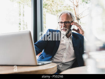 Mature businessman sitting at table in a cafe using cell phone and laptop Stock Photo